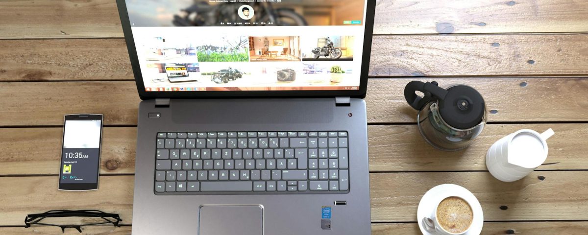 silver laptop next to coffe cup smartphone and glasses